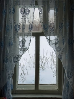 A rustic wooden window with delicate lace curtains in a grandmother's house in a Russian village. The embroidered fabric softly filters the daylight, revealing a serene winter landscape outside. Snow photo