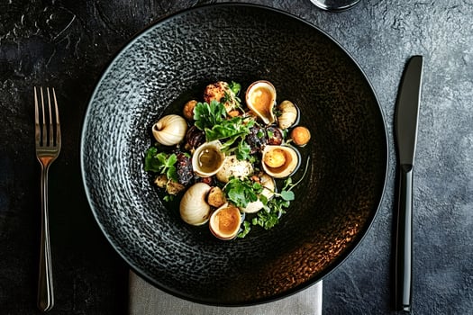 Gourmet escargot dish served on elegant black plate with cutlery photo