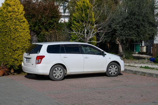 Gaziveren Cyprus -01.03.2025 White station wagon parked under green trees on a sunny day in a peaceful neighborhood photo