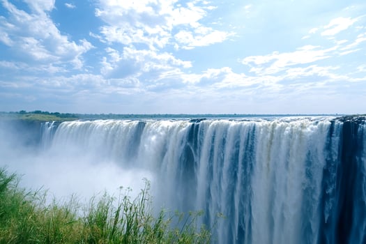 Victoria falls cascading water with mist and blue sky in background photo