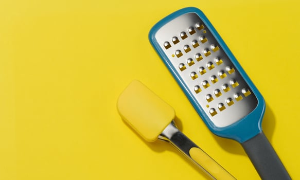 Yellow silicone kitchen tongs and metal vegetable grater on yellow background photo