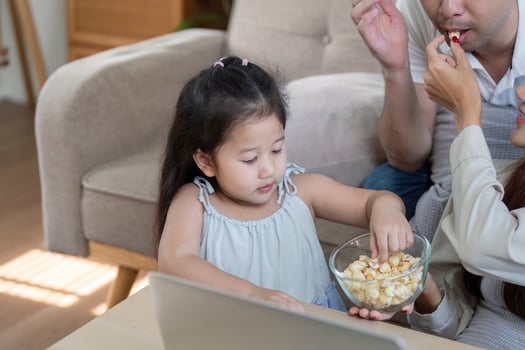 Family sharing popcorn and laughter while watching something on a laptop photo