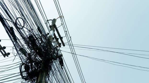 Different communication cables are attached to concrete poles. The chaos of unorganized cable installation in Thailand. under view of clear sky. photo