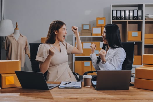 Two women sitting at a desk with boxes and laptops photo