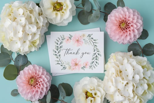Floral arrangement surrounds Thank You card, set against soothing turquoise background photo