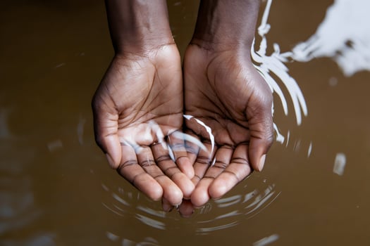 Hands hold clear liquid against a brown background, emphasizing freshness and purity photo