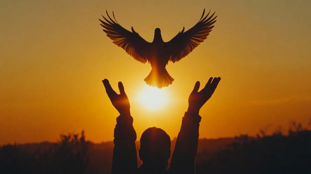 A person with their hands raised as a bird flies overhead during a golden sunset, creating a peaceful silhouette. Open for inspiration. photo