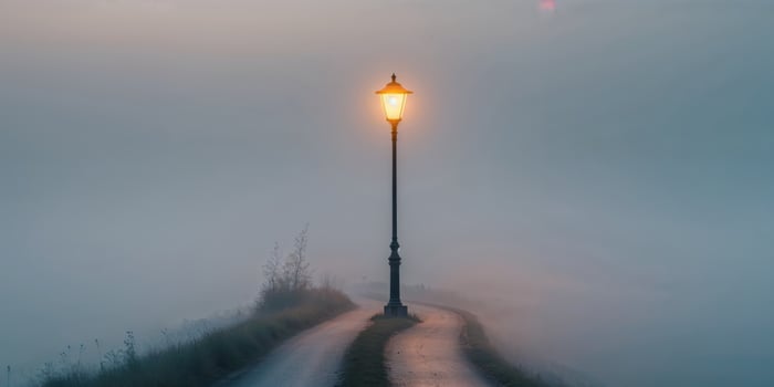 Serene pathway with a glowing lamp post in a foggy landscape during early morning hours. photo
