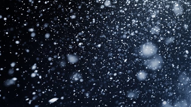 A flurry of bright snow falls against a blurred dark sky. The wintery precipitation is captured in this abstract and atmospheric shot. photo