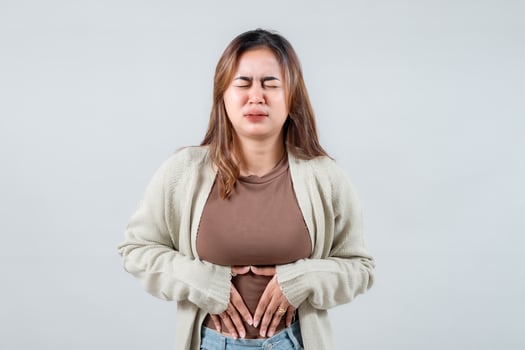An a young woman grimaces uncomfortably while holding her stomach, wearing a comfortable sweater. Her expression suggests pain or anxiety, capturing a moment of incomprehensible distress. photo