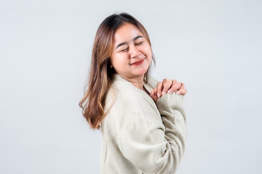 young woman smiles brightly, showcasing her happiness in a cozy sweater against a neutral background, embodying warmth and positivity. photo