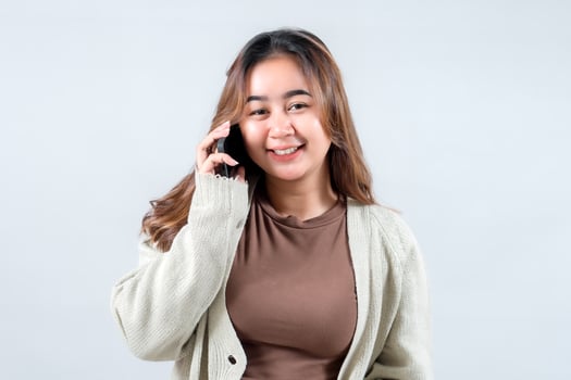 Young woman in a cozy sweater smiles while talking on her mobile phone, conveying connection and communication against a neutral background photo