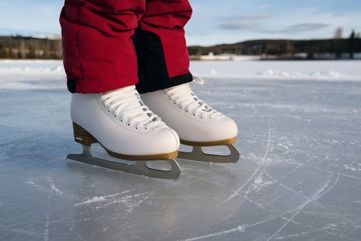 White ice skates with wooden blades on a frozen surface, red pants visible photo