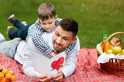 Father Day celebration. Happy dad reading his son's greeting card on picnic in public park photo