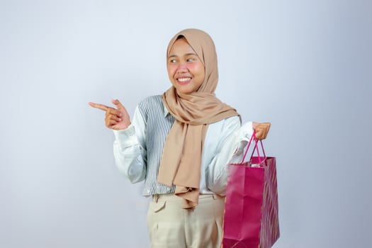 Cheerful Muslim Woman Holding Shopping Bag and Pointing Side photo