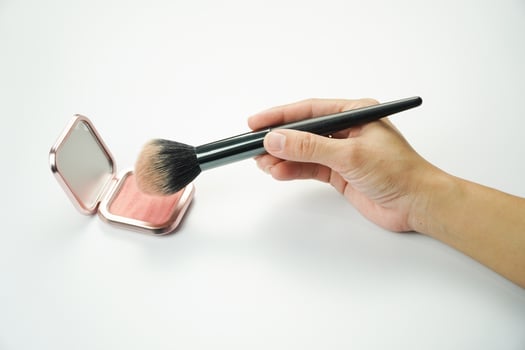 A person holding a brush over a pink blush powder photo