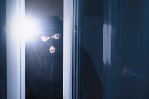 Robbery Concept. Aware masked villain lurking into house through window or glass door, using torch in the dark photo