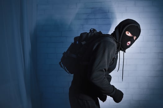 Burglary Concept. Sneaky and scared intruder wearing black balaclava hat lurking in the dark, looking at camera photo