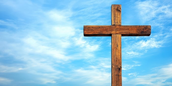 Wooden cross stands against a bright blue sky with clouds during the day photo