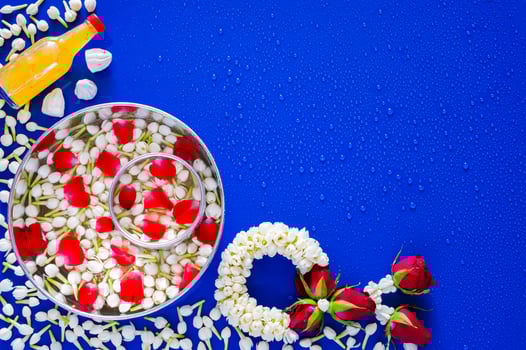 Flowers in water bowl for blessing, scented water and marly limestone with jasmine garland on wet blue background for Thailand Songkran festival background. photo