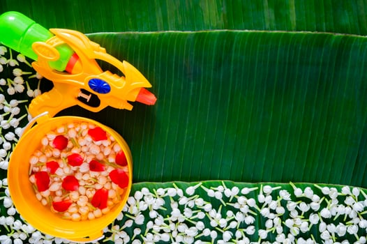 Flowers with water in yellow bucket for blessing with water gun on banana leaves background for Thailand Songkran festival background. photo