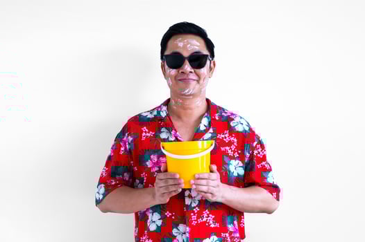 Thai male wearing sunglasses with white clay filler on face wearing colorful shirt holding bucket for Songkran or Water festival in Thailand concept. photo