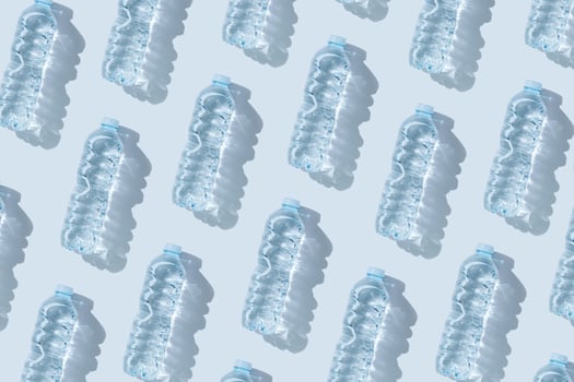 Pattern small plastic bottles with clean drinking water at sunlight, shadow on blue background. Full closed bottle water half litre. Pollution, plastic garbage, non-biodegradable packaging waste photo