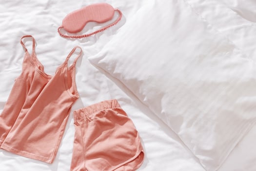 Pink female pajama, sleep eye mask on white bedclothes background. Top view comfort pyjamas for health sleeping. Romance mood, singlet and shorts for girl light pink trend color, pillow blanket photo