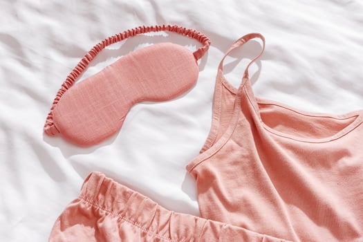 Pink female pajama and sleep eye mask on white cloth bed sheet. Top view comfort pyjamas for health sleeping. Romance mood, singlet and shorts for girl light pink trend color, sleepwear photo