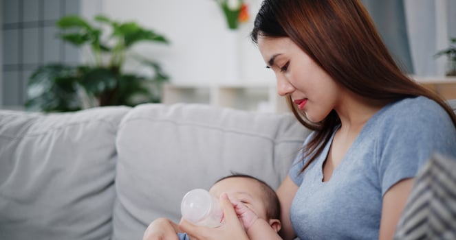 Selective focus shot Beautiful mother gently holds her little son in her arms and feeds him with a bottle while sitting on a sofa in the living room, with an atmosphere full of love and warmth photo