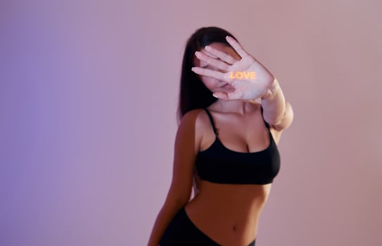 A woman in a black bra top and black pants is holding up her hand photo