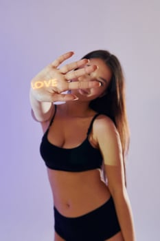 A woman in a black bra top and underwear holding up a neon sign that says love photo