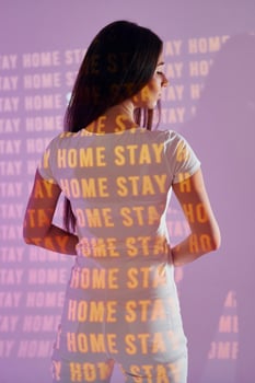 A woman in white shirt standing in front of a wall with the words home stay photo