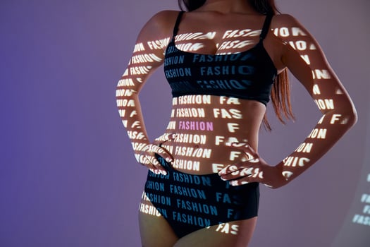 A woman in a bikini top and underwear is holding up a sign that says fashion photo