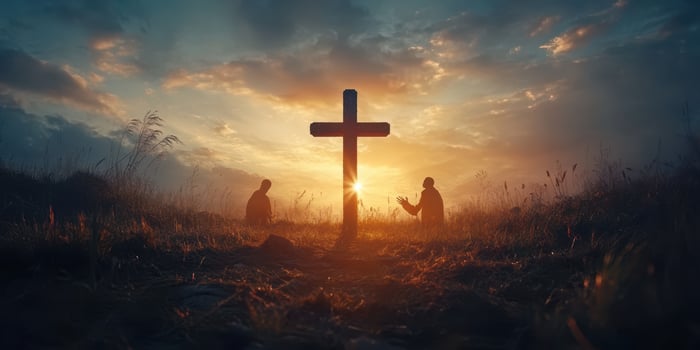Two individuals in prayer at sunset beside a cross in a tranquil field photo