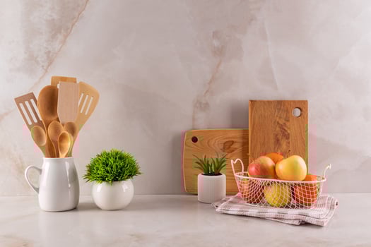 Beautiful kitchen backdrop with a set of wooden kitchen tools and cutting boards on a marble beige countertop with potted plants. A bowl of fruit. photo