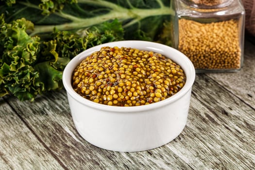 A bowl of mustard and a jar of mustard seeds photo