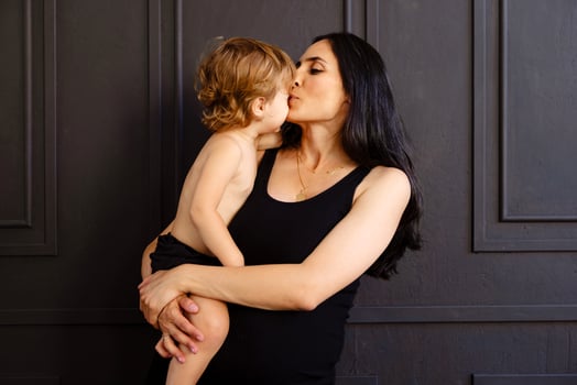 An attractive pregnant woman in a black dress kisses her cute toddler boy. An adorable mom hugs her little child at home. photo