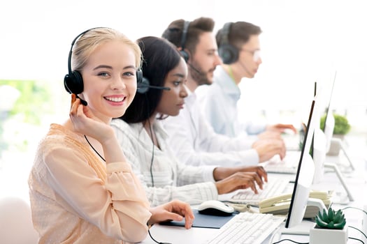 Team of diverse hotline operators with headphones providing service to clients at call center. Young customer support representatives working in telemarketing or telecommunications at modern office photo