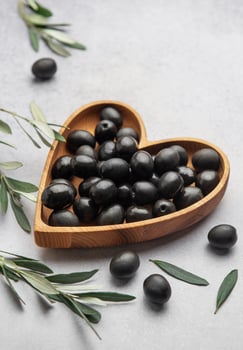 Heart shaped wooden bowl filled with black olives photo