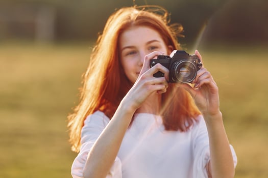 Holding cameras. Young girl is on the field at sunny daytime having nice weekend photo