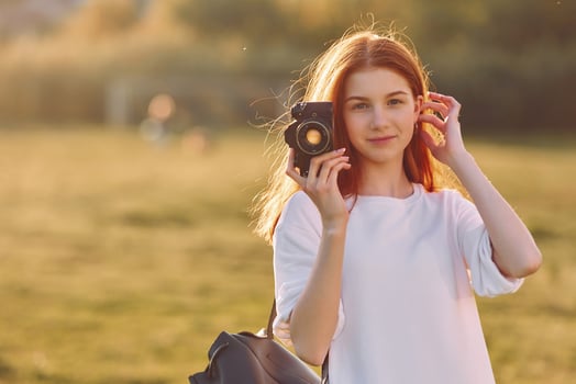 Professional camera in hand. Young girl is on the field at sunny daytime having nice weekend photo