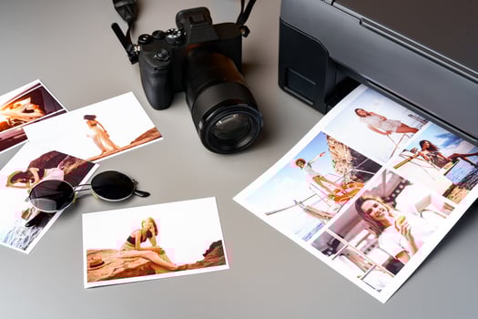 Photo camera with colorful printer photos on gray desk