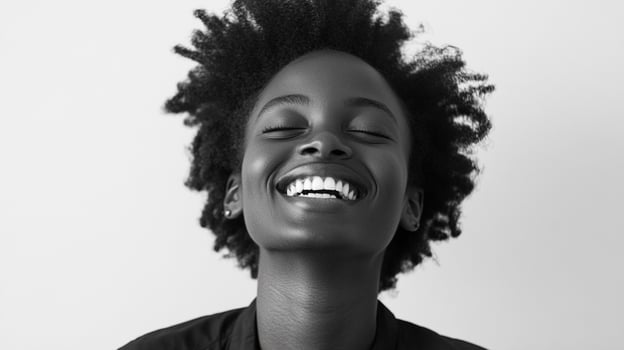 A black and white photo of a young woman smiling with her eyes closed. She is radiantly happy and enjoying a moment of peace.