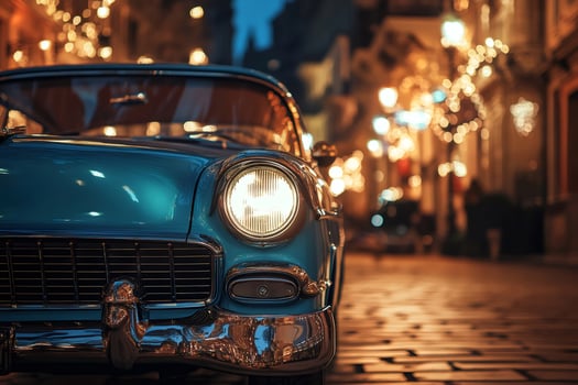 Classic blue car parked on cobblestone street at night with city lights reflecting on hood photo