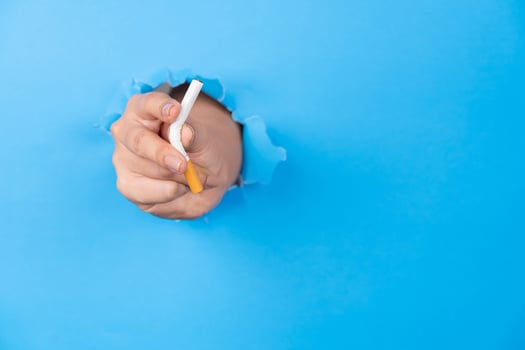 Hand holding cigarette through hole in blue paper photo