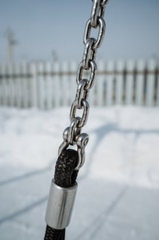 A closeup of a heavyduty metal chain attached to a sturdy rope, set against a winter landscape that showcases the seasons charm and invites appreciation for the outdoors photo