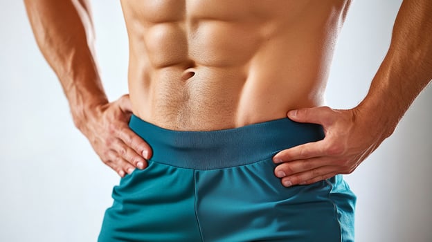 Torso of a fit man showcasing defined abdominal muscles, hands on hips, wearing teal shorts. Strength and fitness concept. photo