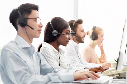 Line of call centre representatives with headsets working on computers at open space office. Group of hotline operators managing customer's claims online, space for text photo