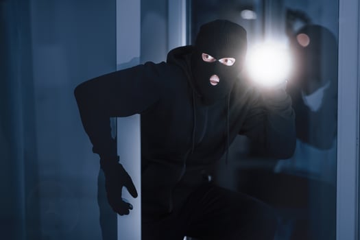 Time For Crime. Cautious burglar looking and peeping into building through window or glass door with torch photo